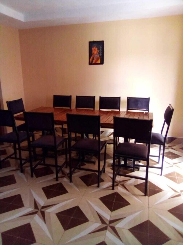 A dining area with a wooden table and chairs, a tiled floor, and a framed picture on the wall.