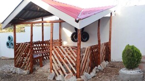 Un espace extérieur aménagé dans un style rustique, avec un toit en métal, entouré de rampes en bois et agrémenté d’une petite plante en pot.
