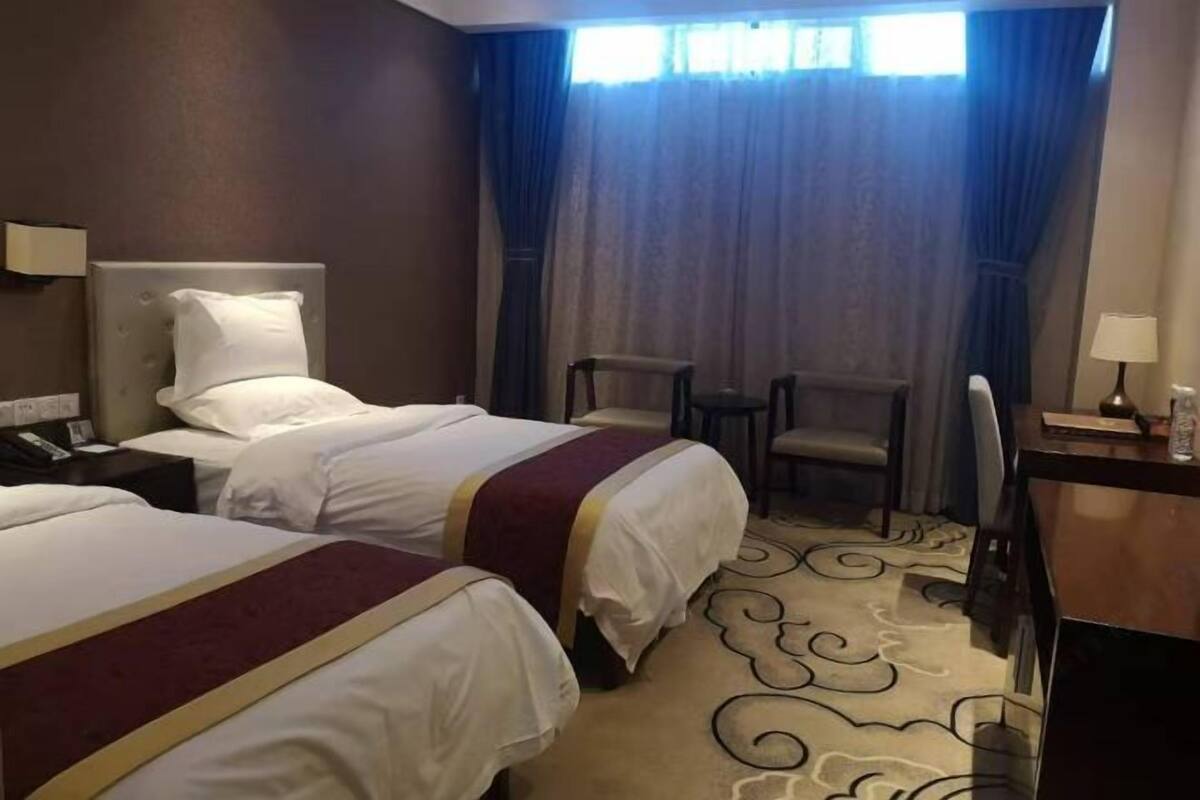 A hotel room with two beds, a desk, a chair, and a window with curtains.