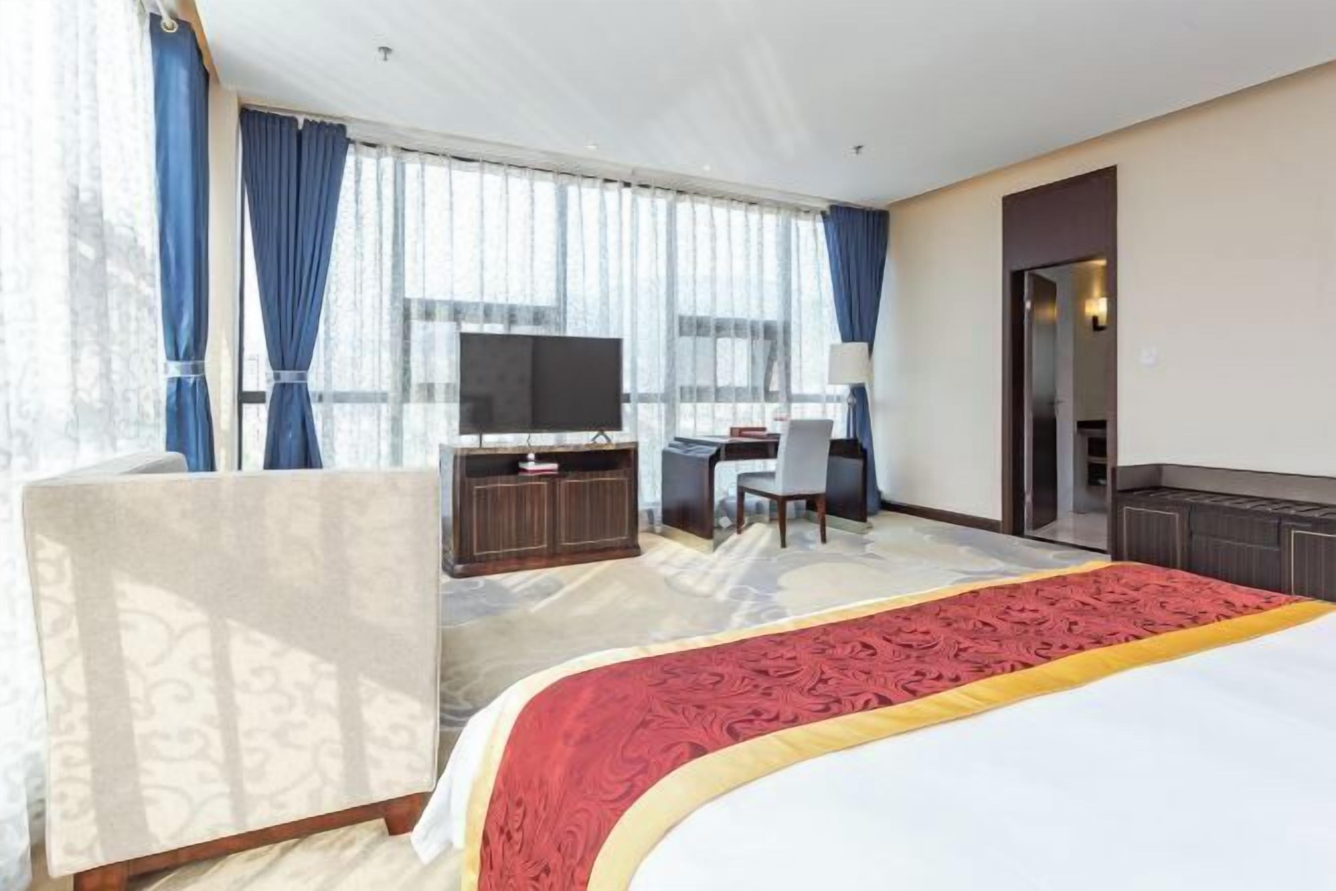 Ein Hotelzimmer mit einem großen Bett, einem Schreibtisch mit Stuhl, einem Fernseher und einem Kleiderschrank.