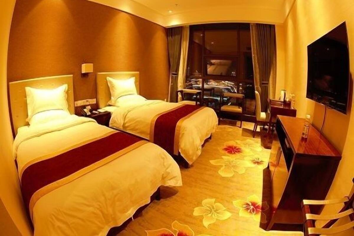 A hotel room with two beds, a desk, a TV, and a view of the city.