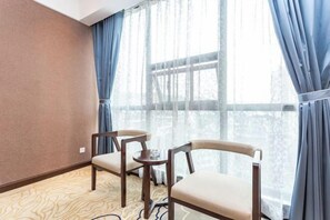 A hotel room with two wooden chairs, a small round table, and a large window with blue curtains. - Tianrui Hotel (Yanhe)