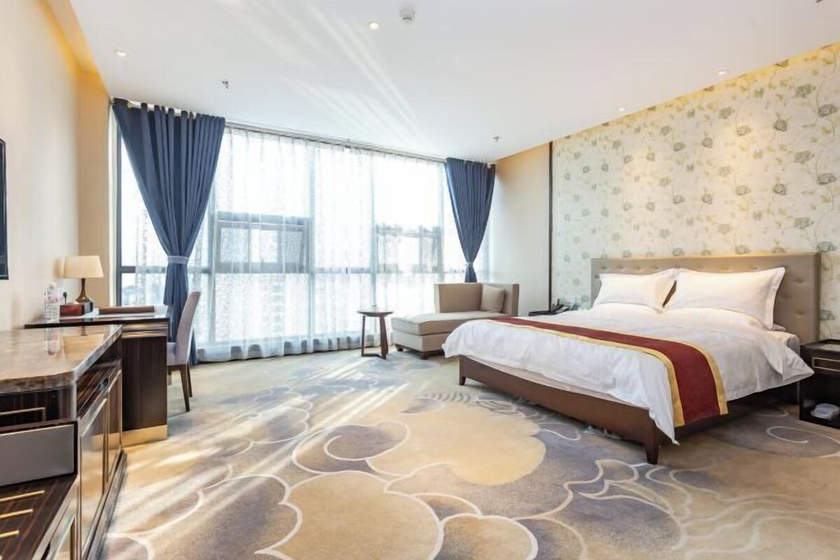 A hotel room with a large bed, a desk, a chair, and a small table.