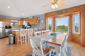 A modern kitchen with wooden cabinets, a stainless steel refrigerator, and a large island with white chairs. - Sea Blue: 4-Bedroom Oceanside w/ Private Pool and Hot Tub (Corolla)