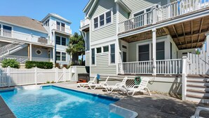 A swimming pool with a white deck and lounge chairs, surrounded by a white picket fence and a two-story house with a balcony. - Anchors Down: Private Pool | Hot Tub | Rec Room (Corolla)