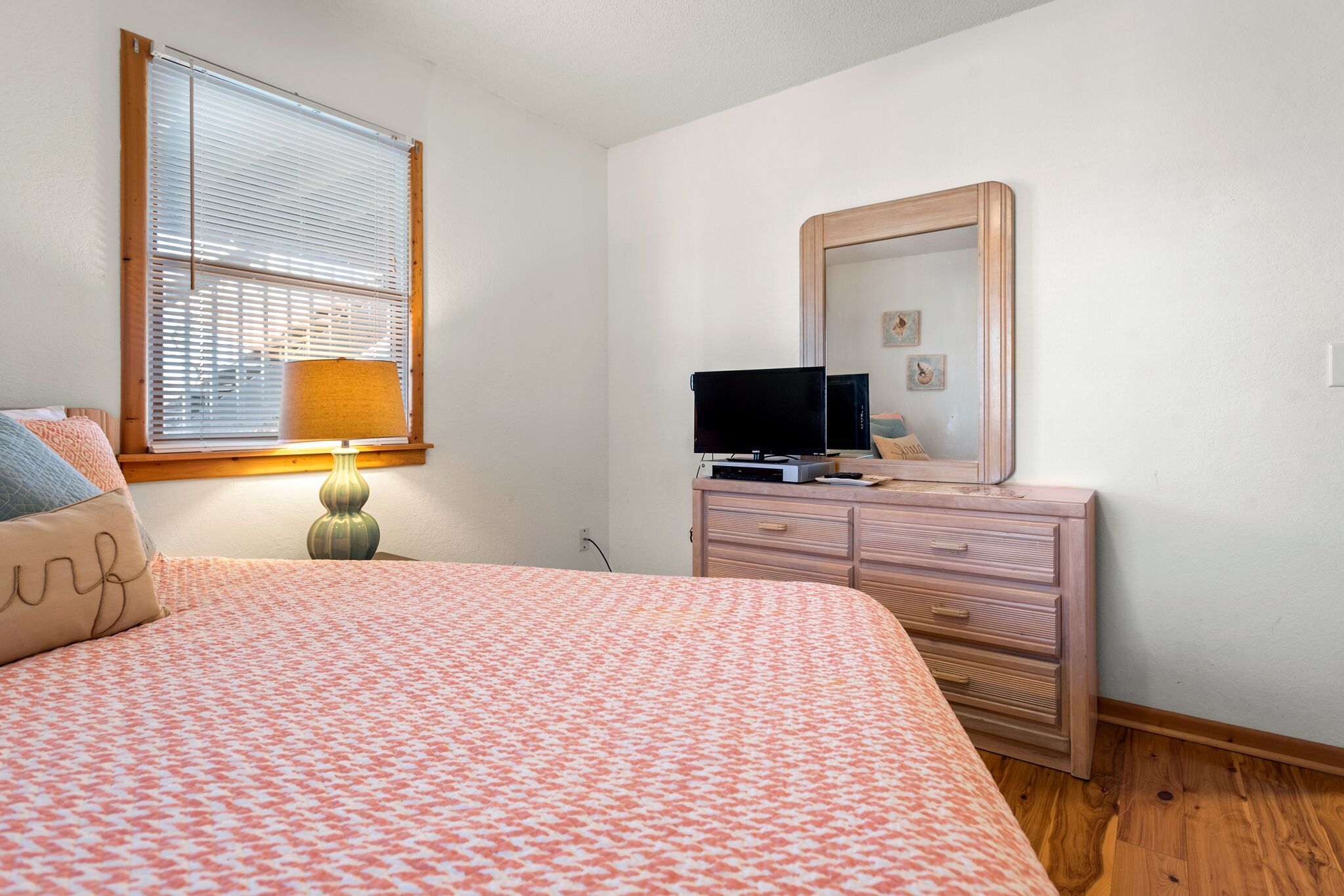 A bedroom with a bed, a dresser, a mirror, and a window with blinds.
