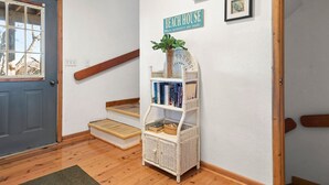 A staircase with a white wicker bookshelf against a wall, a door, and a sign that reads "BEACH HOUSE." - Kiki's Retreat: Walk to Duck Village | Pets OK (Duck)
