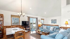 A spacious living room with a wooden dining table, blue sofa, and a television. - Kiki's Retreat: Walk to Duck Village | Pets OK (Duck)