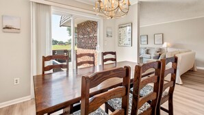 Un coin repas avec une table et des chaises en bois, un lustre et une vue sur une terrasse en briques, visible à travers des portes vitrées.