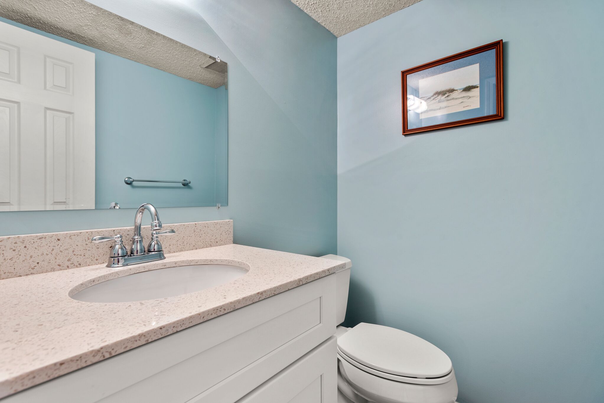 A bathroom with a white sink, a mirror, a framed picture on the wall, and a white toilet.