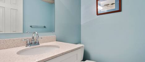 A bathroom with a white sink, a mirror, a framed picture on the wall, and a white toilet.