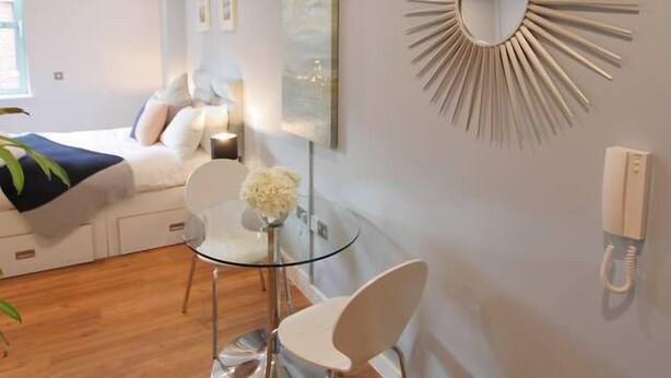 Een moderne slaapkamer met een bed, nachtkastje en een spiegel aan de muur.