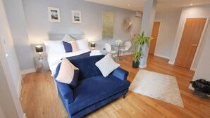 Een moderne hotelkamer met een blauwe bank, een bed met witte beddengoed, een kleine ronde tafel met stoelen, en een plant in een pot.