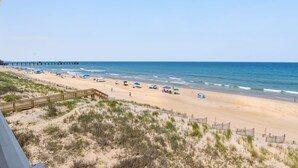 Ein Strand mit einer Holzpromenade, Sandstrand und einem Pier in der Ferne.
