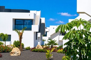 Un bâtiment moderne doté d’une grande fenêtre, d’une façade blanche et entouré de verdure.