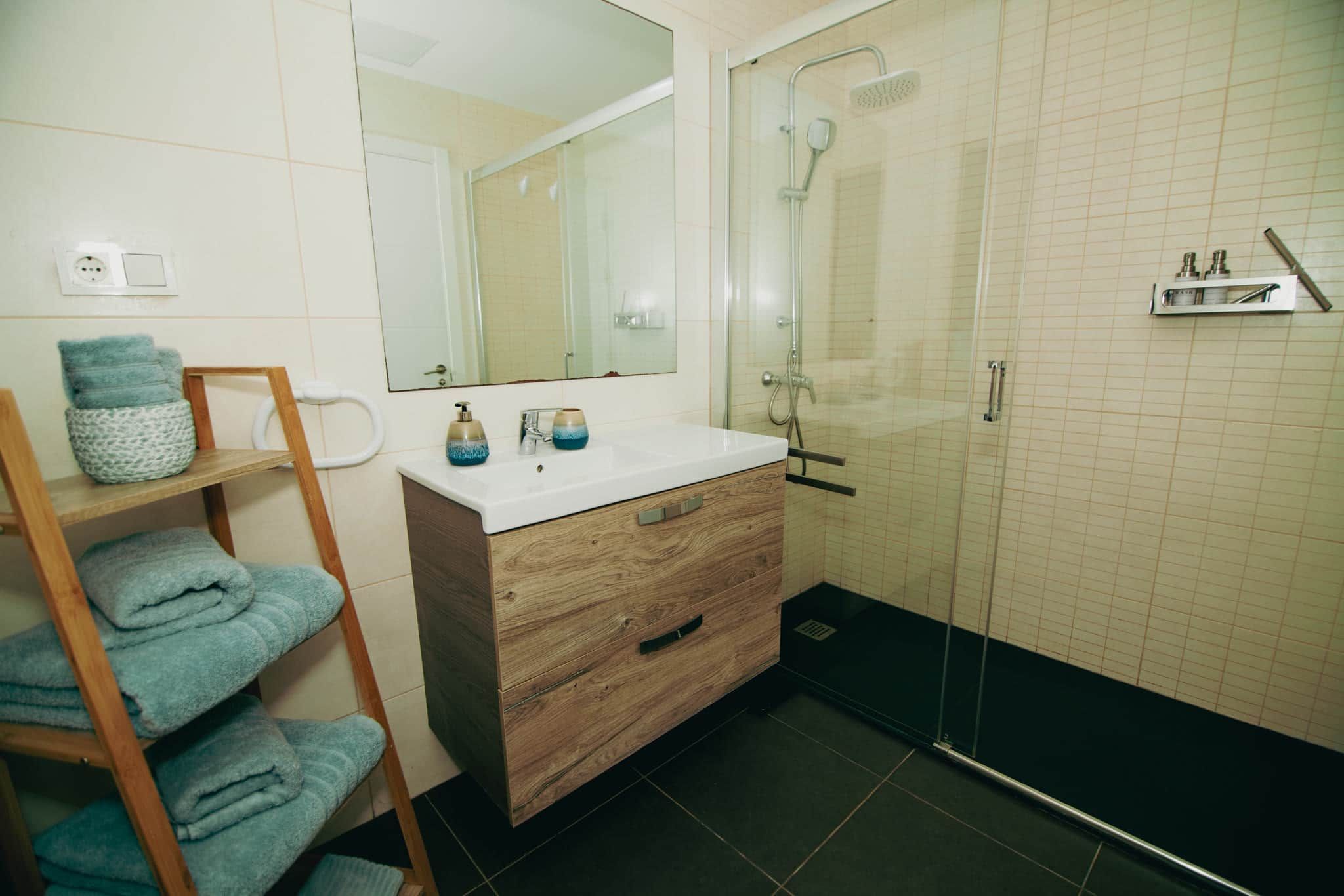 Een badkamer met een houten wastafelmeubel, een douchecabine met glazen wanden en een handdoekrek met opgevouwen handdoeken.