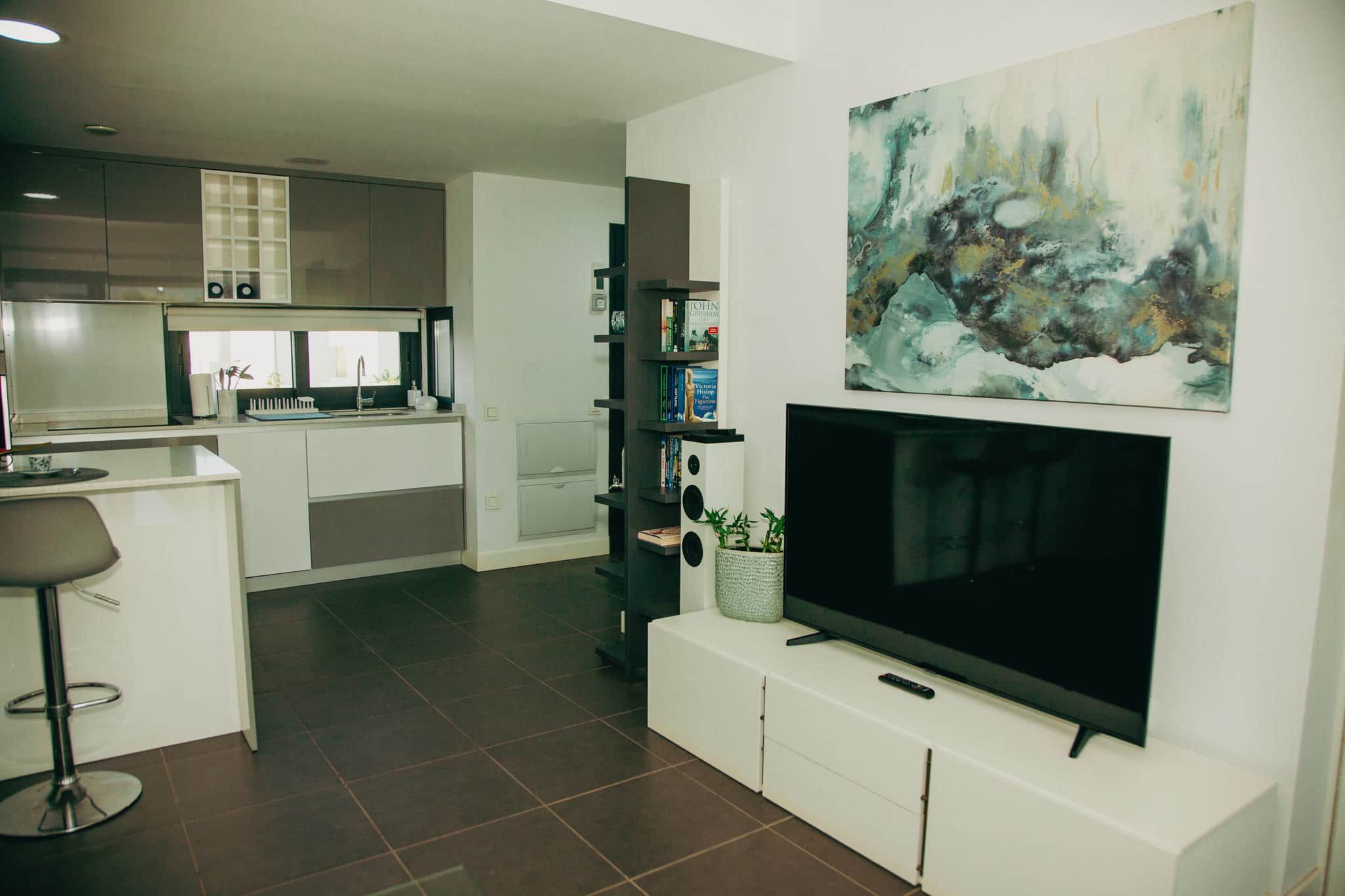 A modern kitchen with a built-in microwave, a dining area with a bar stool, and a living room with a flat-screen TV and abstract art.