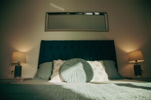 A neatly made bed with a dark headboard, two bedside lamps, and a framed picture above.