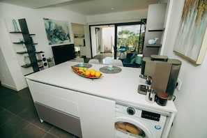 A compact kitchen with a built-in washing machine, a coffee machine, and a fruit bowl on the counter. - Luxury Penthouse: Terrace, Hot Tub and Sauna (La Oliva)