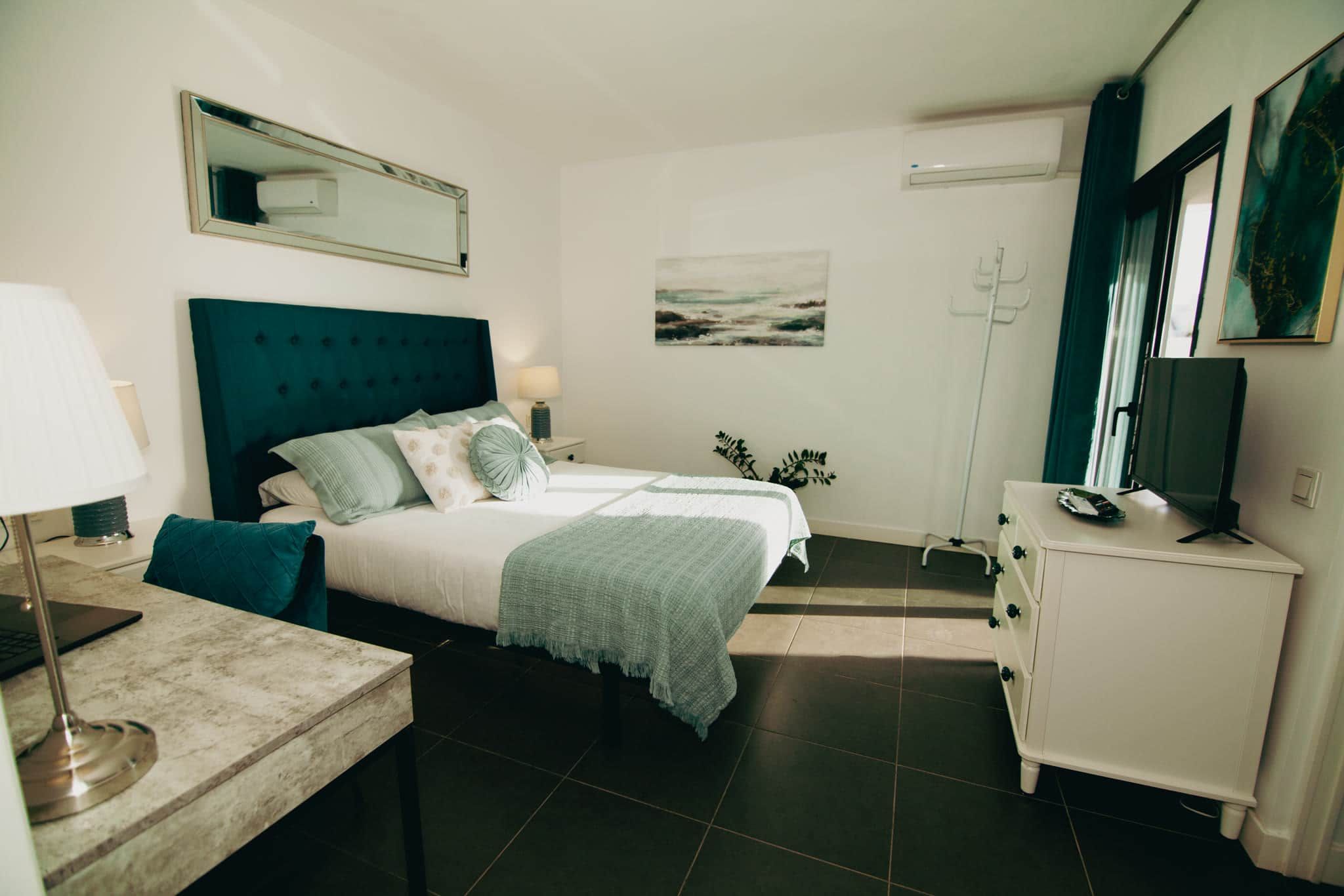 Een hotelkamer met een bed, nachtkastje, lamp, kaptafel en een schilderij aan de muur.