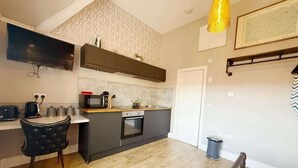 Una cocina compacta con electrodomésticos modernos, un comedor con una silla negra y un pequeño cubo de basura.
