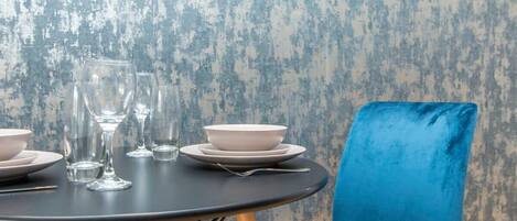 A round dining table with plates, glasses, and cutlery. A blue chair is positioned to the right.