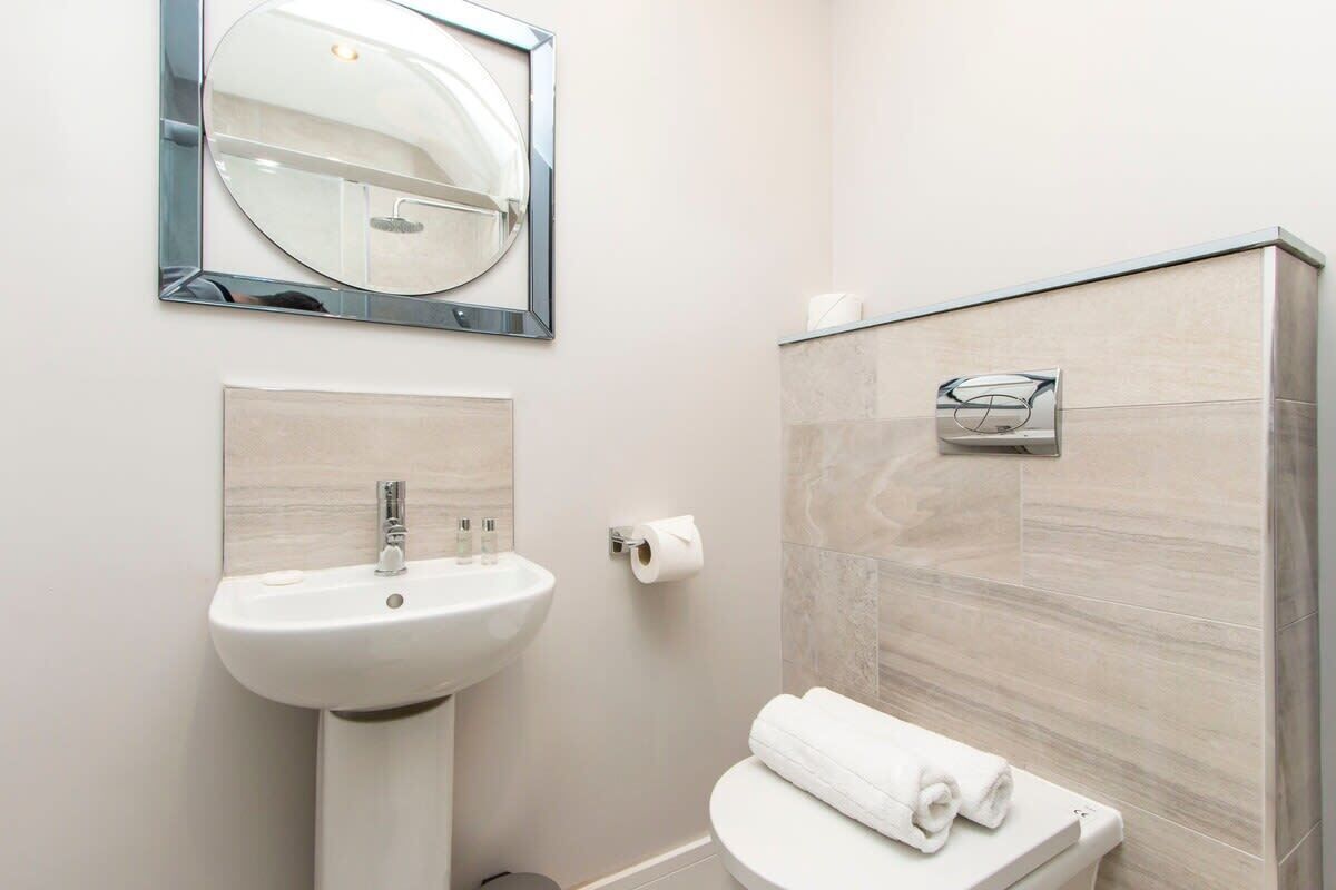 Un baño con lavamanos pedestal, inodoro, toallero y espejo.