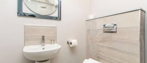 Un baño con lavamanos pedestal, inodoro, toallero y espejo.