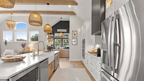 Una cocina moderna con un refrigerador de acero inoxidable grande, armarios blancos y una isla central con un cuenco tejido.