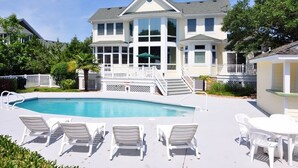 Ein großes Haus mit Swimmingpool, weißer Gartenmöbeln und einer überdachten Terrasse.