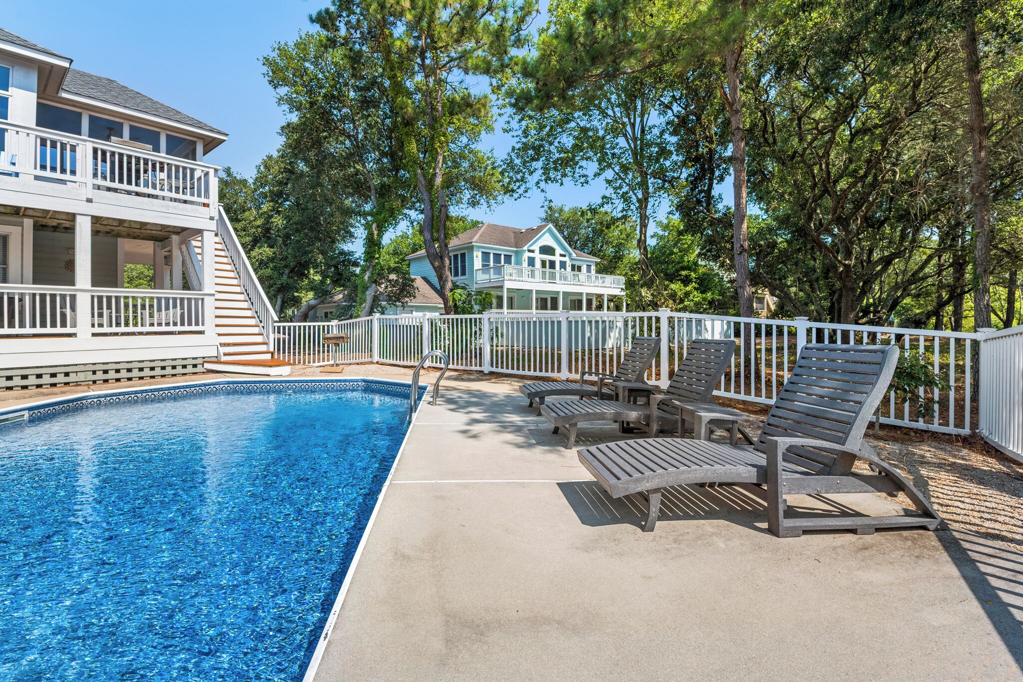 A swimming pool with lounge chairs and a white fence.