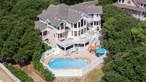 Une grande maison à plusieurs étages, dotée d’une piscine et entourée d’une végétation dense.