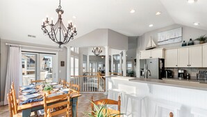 A spacious kitchen with white cabinetry, a central island, and a dining area with wooden furniture. - It's 5 O'clock Somewhere: Pool, Spa, Club Access (Corolla)