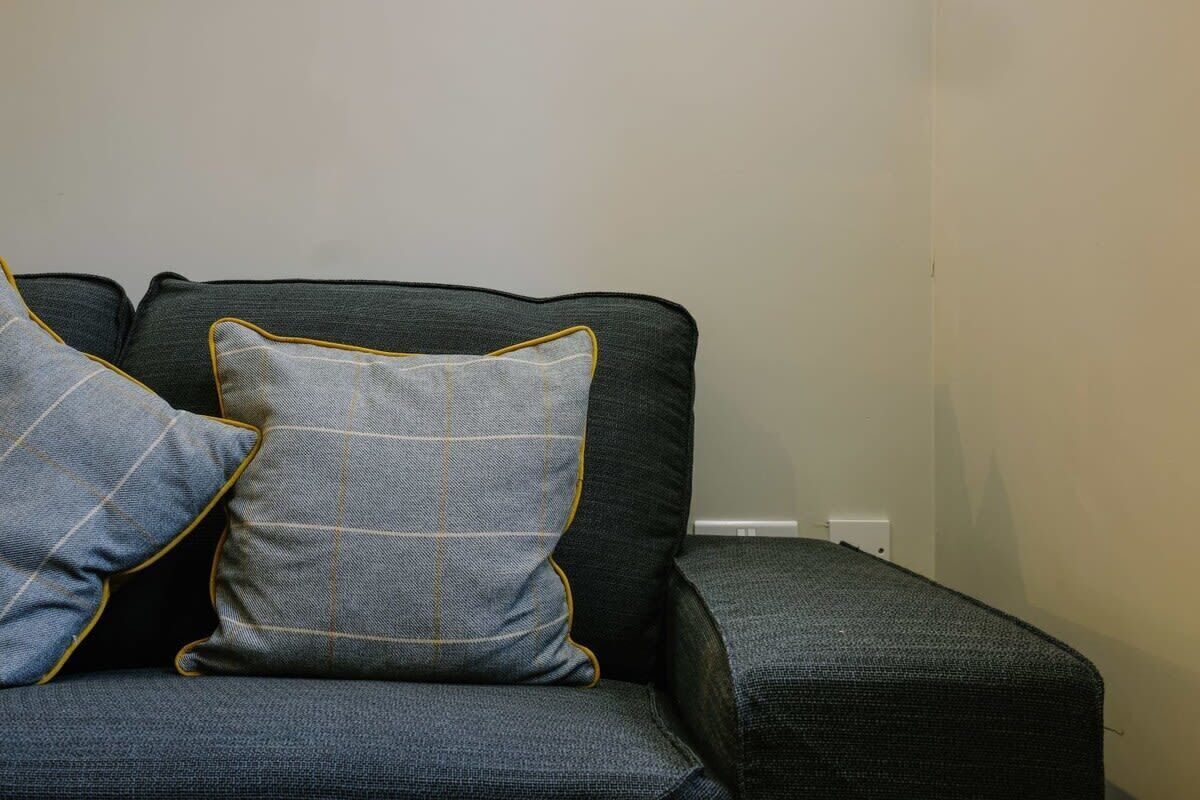 A dark grey sofa with two matching cushions, one with a yellow trim.