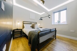 A modern bedroom with a bed, bedside tables, a window, and a ceiling light fixture. - One Bedroom Apartment in Fantastic Location (Bristol)