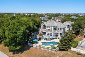 Stunning multi-story residence with a wrap-around balcony, pool, and lush greenery.