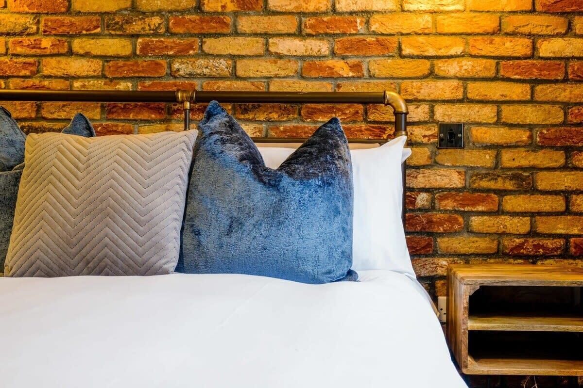 Un lit avec une tête de lit en bois adossée à un mur de briques.