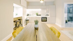 A modern kitchen with white cabinets, a wooden dining table, and yellow chairs. - One Bedroom Apartment Close to MOD (Bristol)