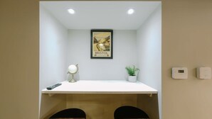 A small, modern room with a white desk, two dark wooden chairs, a framed picture of Bristol, a small potted plant, a desk lamp, and two wall-mounted thermostats. - One Bedroom Apartment Close to MOD (Bristol)