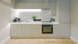 A modern kitchen with white cabinetry, a built-in oven, and a stainless steel sink. - One Bedroom Apartment Close to MOD (Bristol)