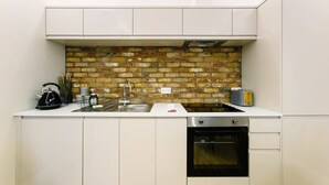 A modern kitchen with white cabinets, a brick backsplash, a sink, a stove, and a toaster. - One Bedroom Apartment Close to Cribbs Causeway! (Bristol)