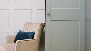 A beige armchair with a dark blue pillow against a white wall with a door. - One Bedroom Apartment Close to Cribbs Causeway! (Bristol)