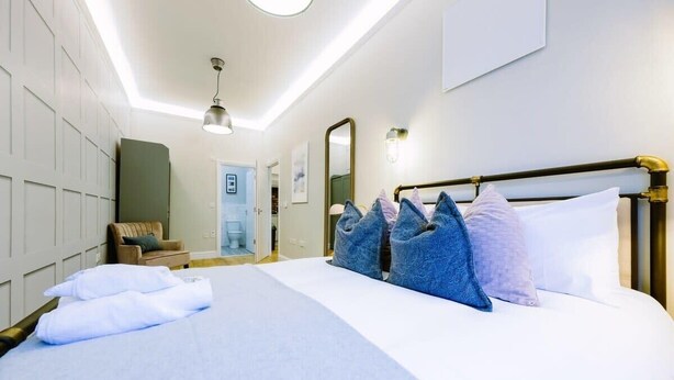 A hotel room with a large bed, a wooden headboard, and a seating area with a chair and a small table. - One Bedroom Apartment Close to Cribbs Causeway! (Bristol)