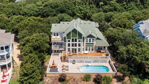 Une grande maison à plusieurs étages, dotée d’une piscine et entourée d’une végétation dense.