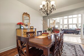 Un coin repas avec une table en bois, des chaises, un lustre et un miroir.