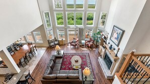 Un salon spacieux, doté d’un grand canapé d’angle, d’une cheminée et offrant une vue sur l’extérieur grâce à de grandes fenêtres.