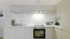 Uma cozinha moderna com armários brancos, forno embutido, pia e chaleira na bancada.