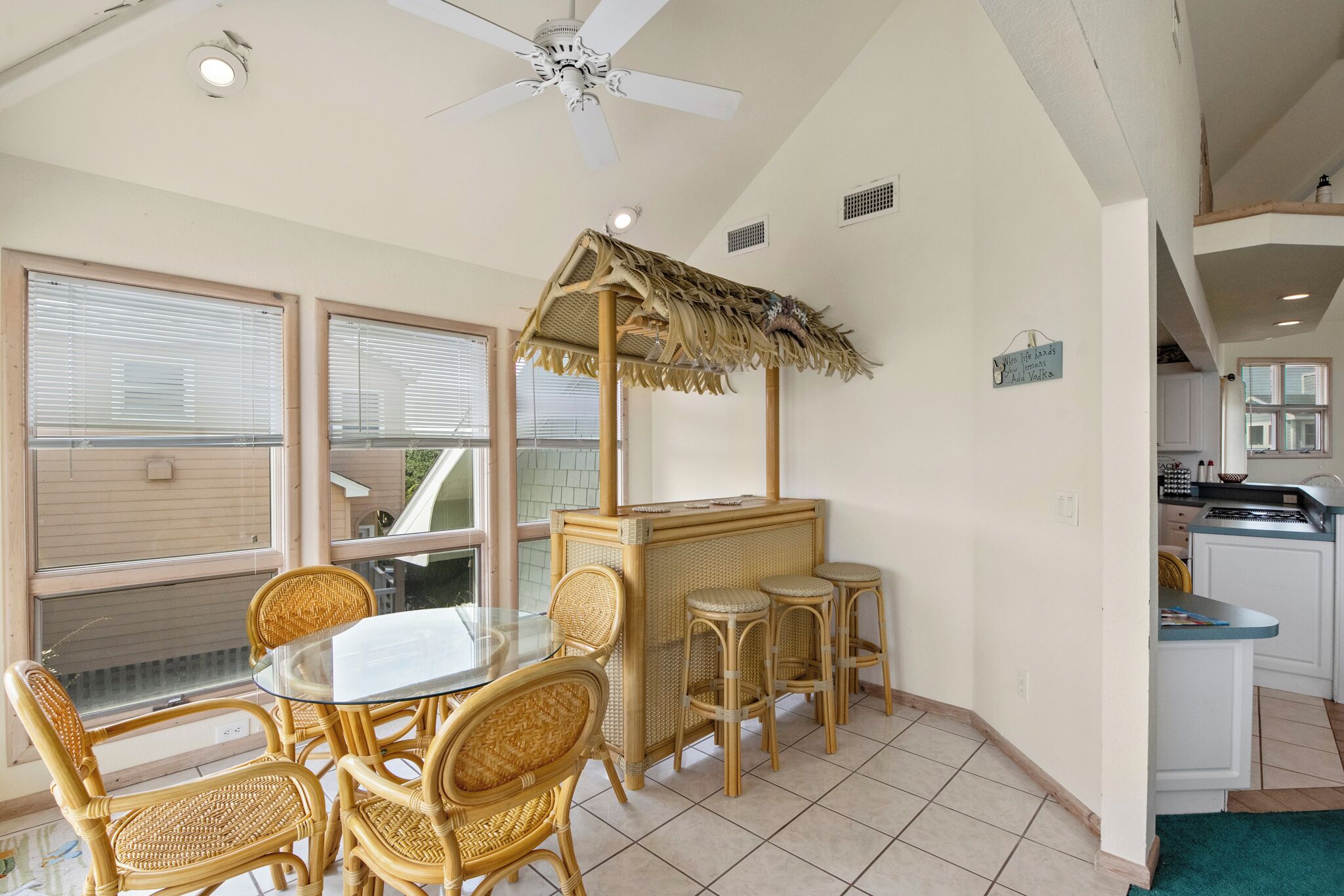 A dining area with a glass table and wicker chairs, a ceiling fan, and a thatched structure.