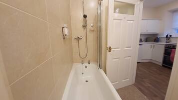 Un baño con bañera, ducha e inodoro. Se ve una cocina al fondo.