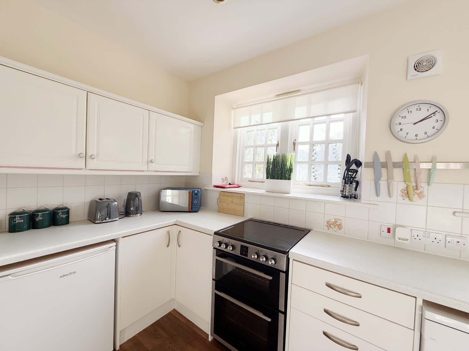Cocina compacta con armarios blancos, estufa, horno, microondas y ventana con vistas a zonas verdes.